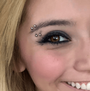 Piercing multiplo sopraccigliare con gioielli metallici su una ragazza sorridente.